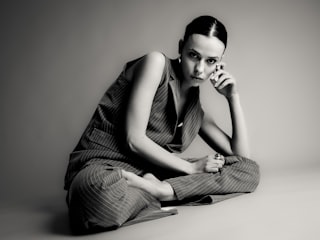 A woman in a pinstripe suit sits with legs crossed.
